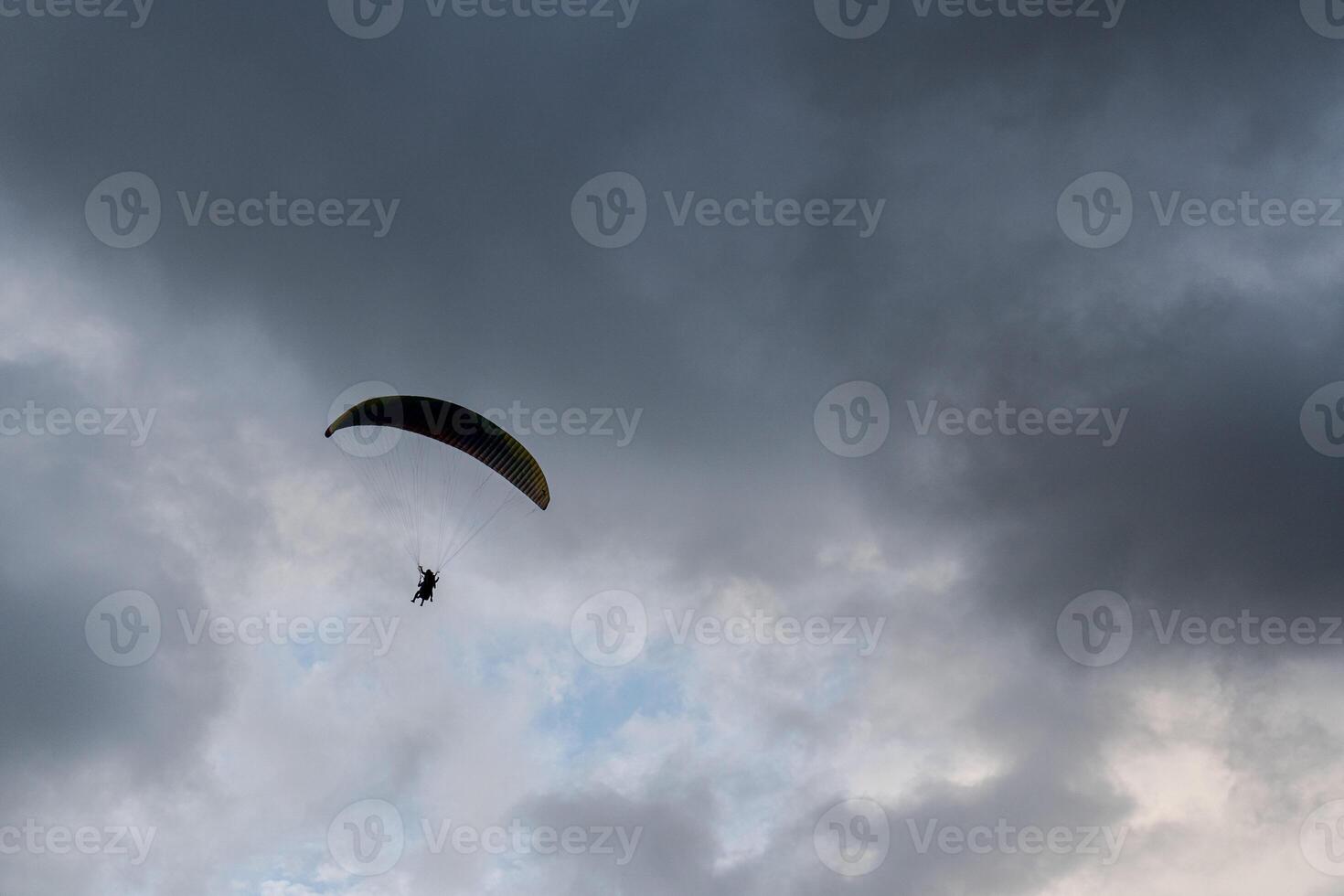 A paraglider soars against a dramatic sky filled with dark and light clouds. photo