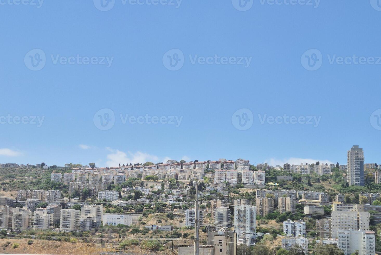 A panoramic view of hillside residential buildings stacked along green slopes, with blue sky creating a peaceful urban landscape photo