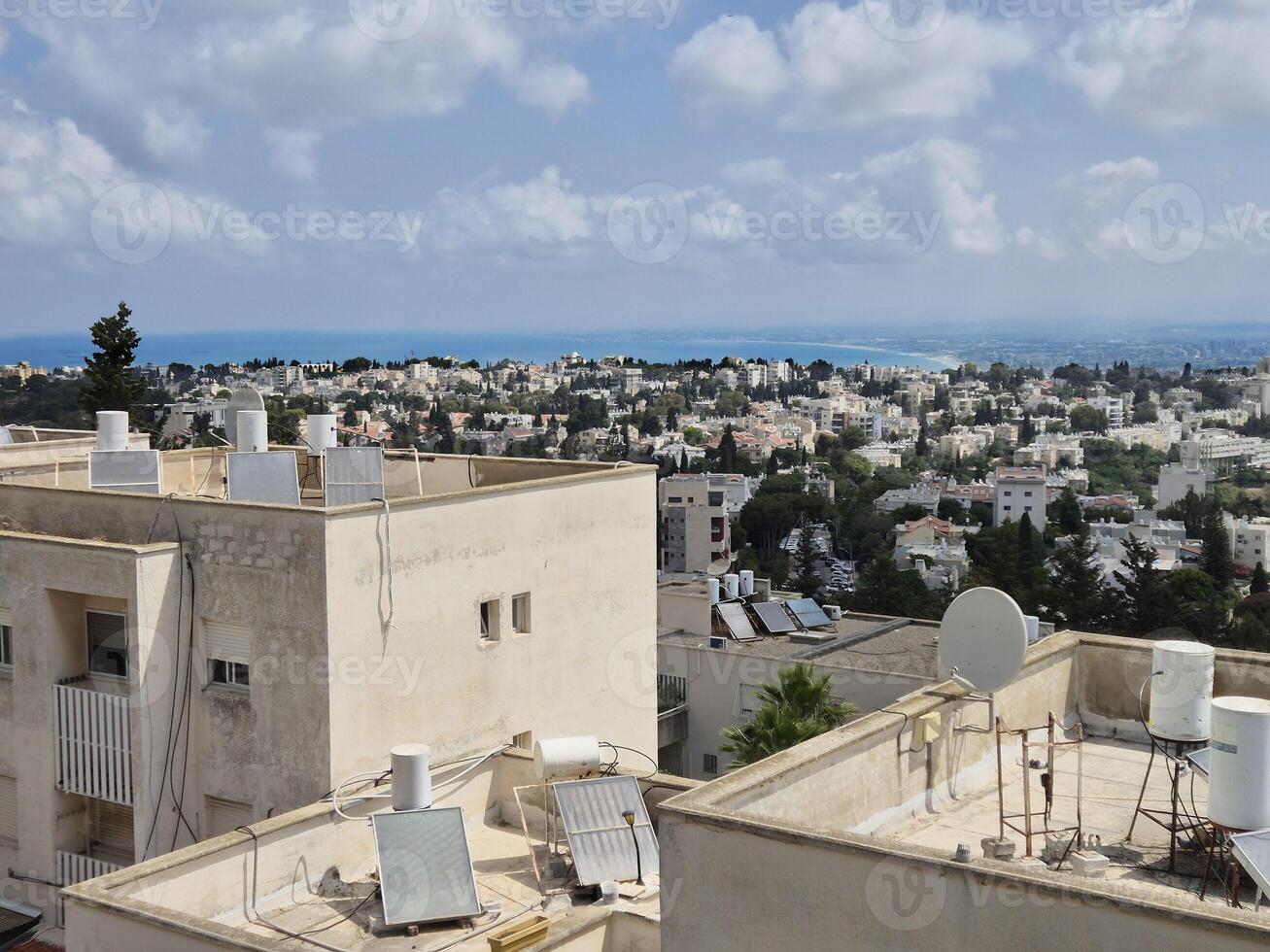Scenic rooftop view of white buildings and residential blocks with a backdrop of sea and distant blue skyline under partly cloudy skies photo