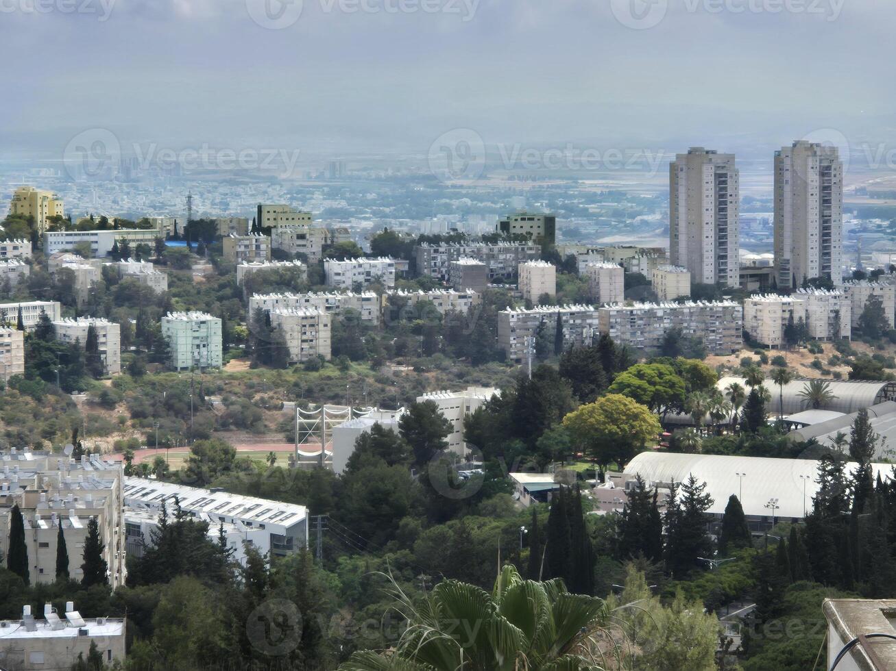 Urban neighborhood filled with residential buildings and greenery, with twin towers and mountain backdrop stretching toward a distant horizon photo