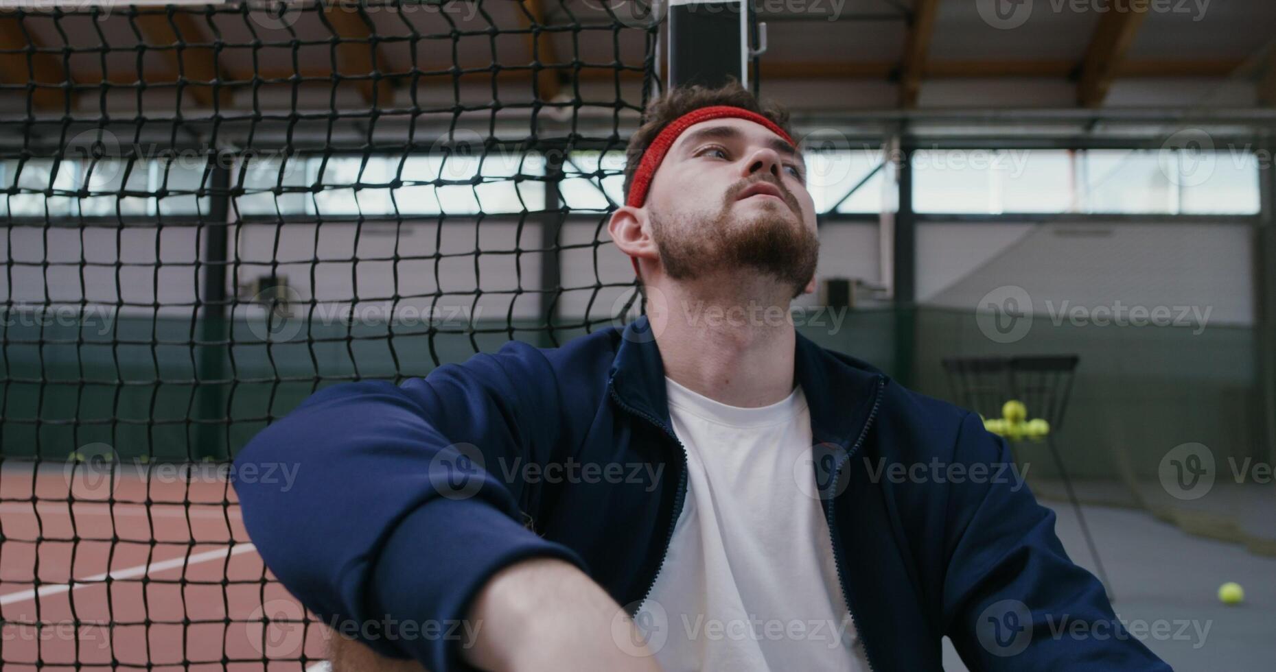 A young man is resting after training, leaning his back and head on a tennis net stretched in the middle of the court, close-up photo