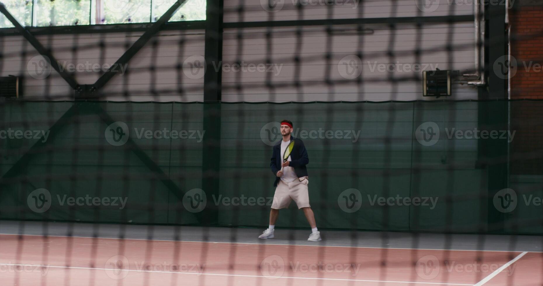 The young man of European appearance plays big tennis, hitting the ball with a racket over and over again, bouncing with each racket hit, filming through the net, the drawing of the net is visible photo