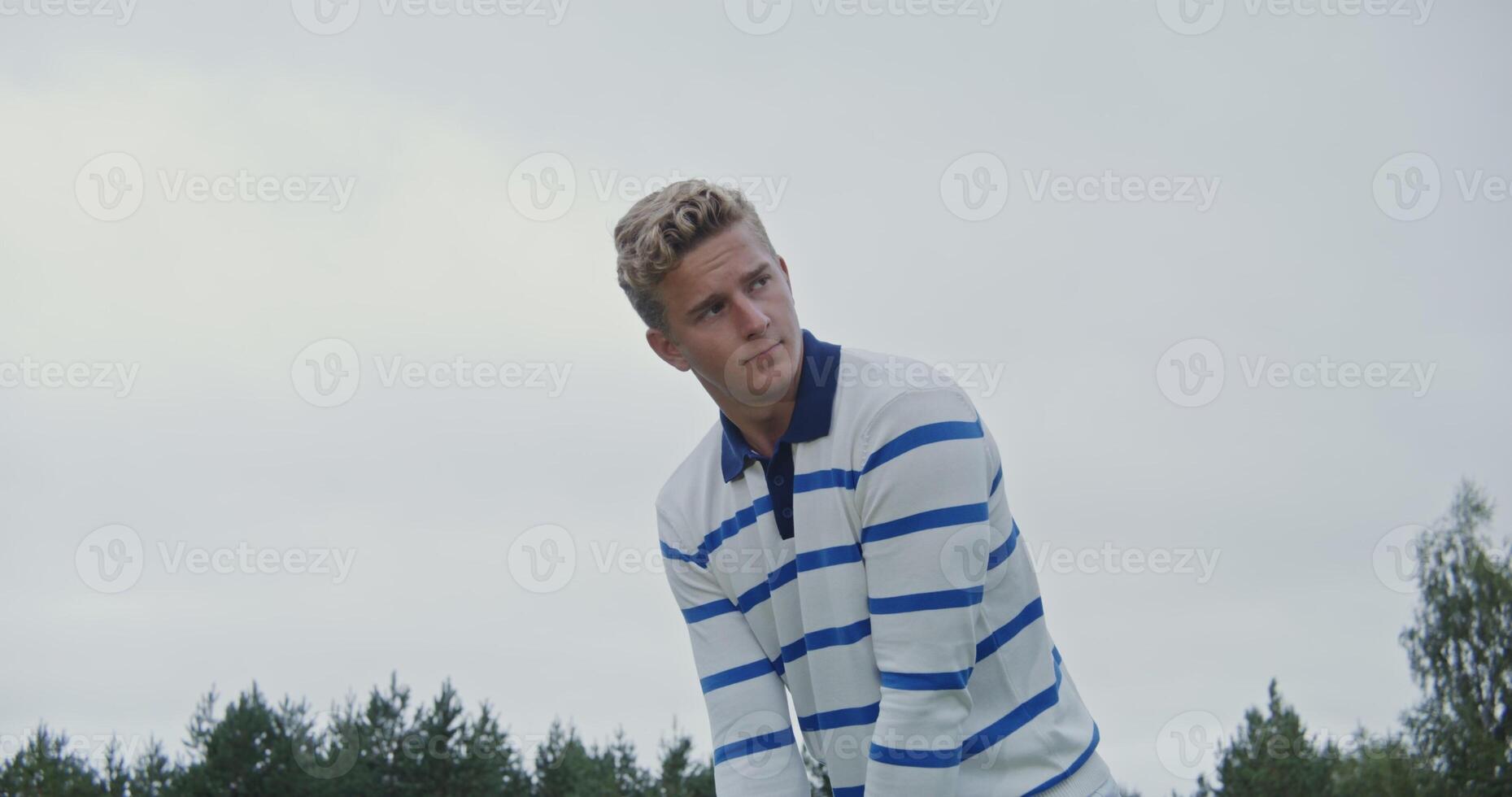 A young man, dressed in white clothes, prepares to hit the ball with a golf club, peering into the distance photo