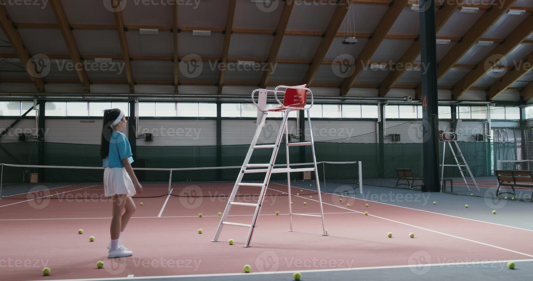 Young woman tennis player of Asian appearance in a short skirt climbs the stairs to a special referee chair, standing in the middle of a tennis court photo