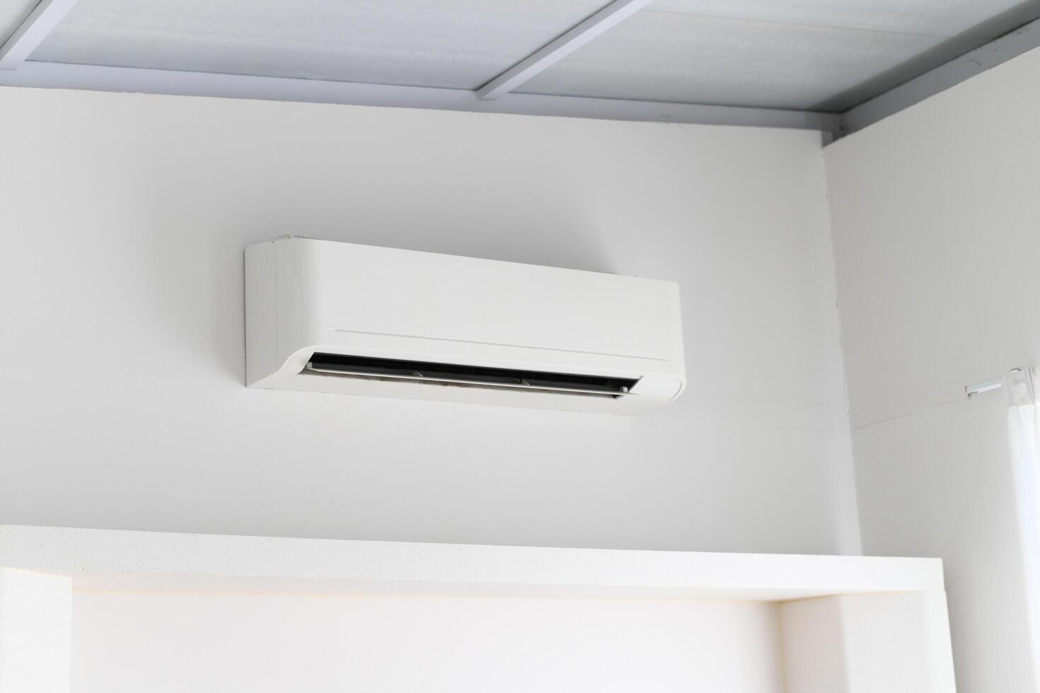 White air conditioner mounted on plain white wall inside bright room. Appliance provides cool air for comfort during hot temperatures. Creates relaxing environment in home or office interior photo