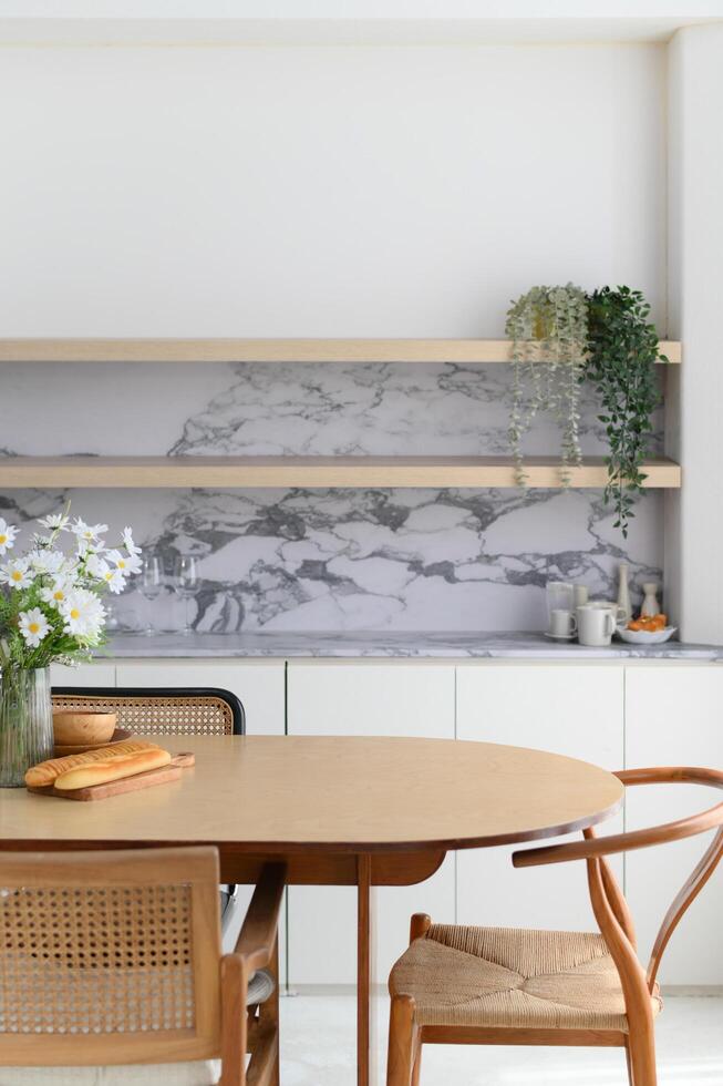 Bright modern dining room interior with wooden table and rattan chair positioned near kitchen area with marble backsplash creating an inviting space for peaceful moments at home photo