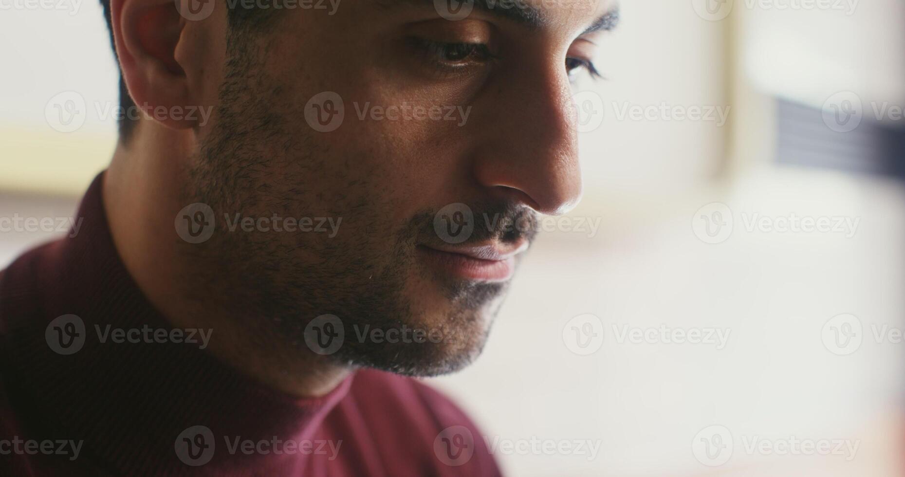 Young black haired man with thick stubble on his face inhales the aroma of coffee with pleasure and takes a sip, close up in profile photo