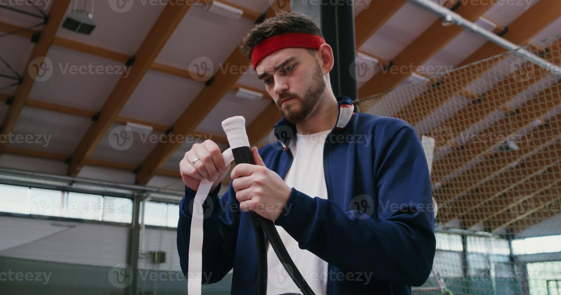 A young man of European appearance wraps the handle of a tennis racket with a special tape, for better grip with his hand, preparing for a tennis match, close up photo