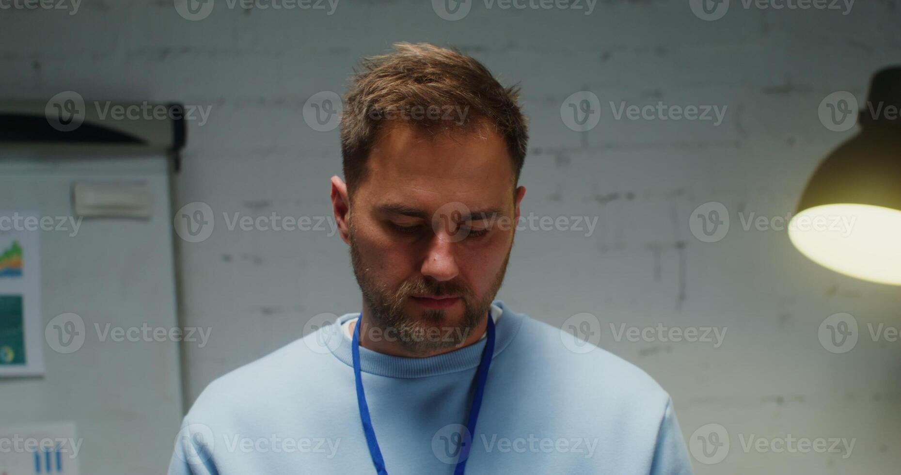 Handsome young man of European appearance with a short beard raises his head and starts smiling while looking straight into the camera, close up of a male face, videotaping in the office photo