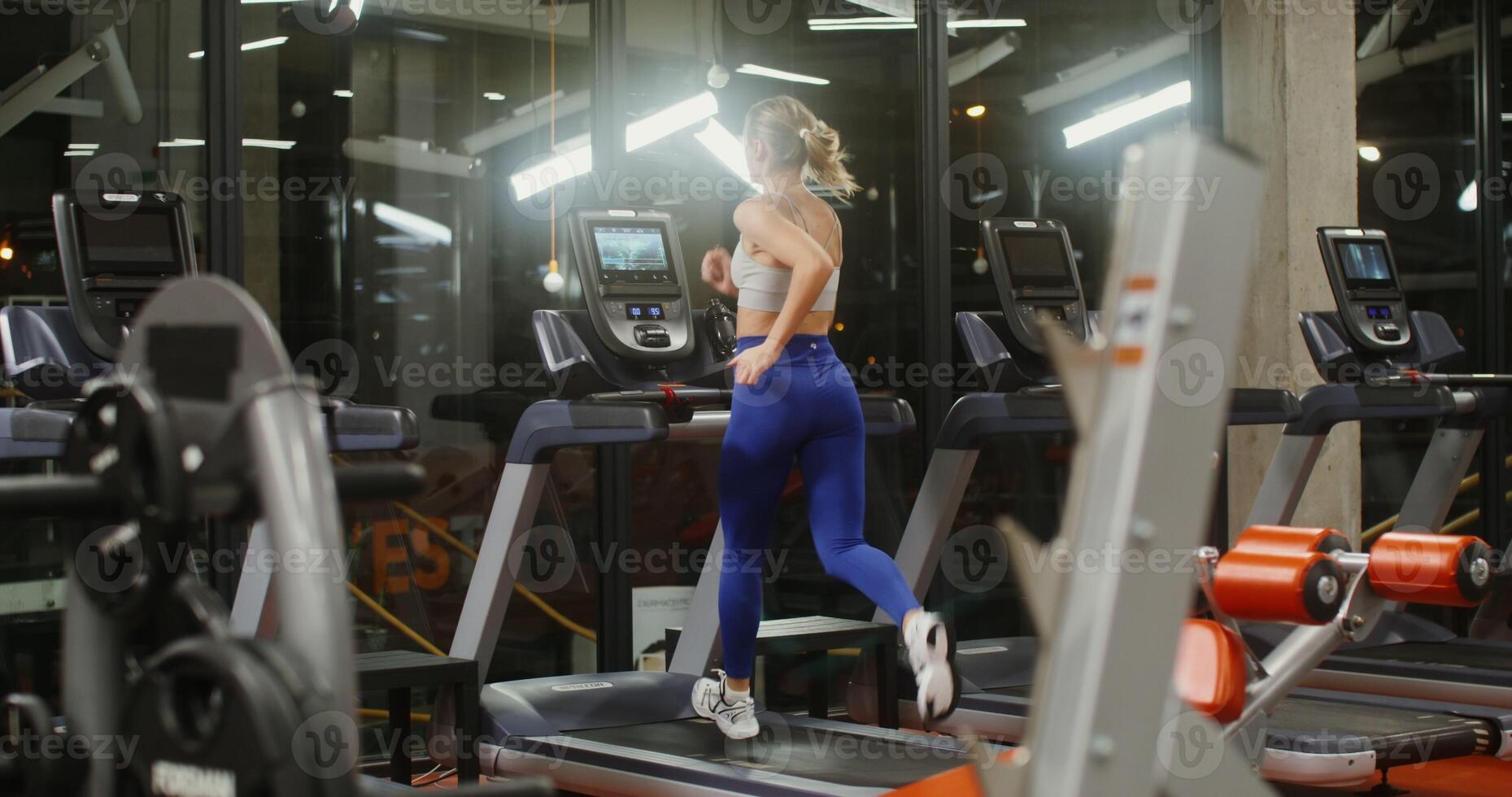 Workout in a well equipped gym on a modern treadmill with integrated display. Young woman running on a treadmill, view from the back photo