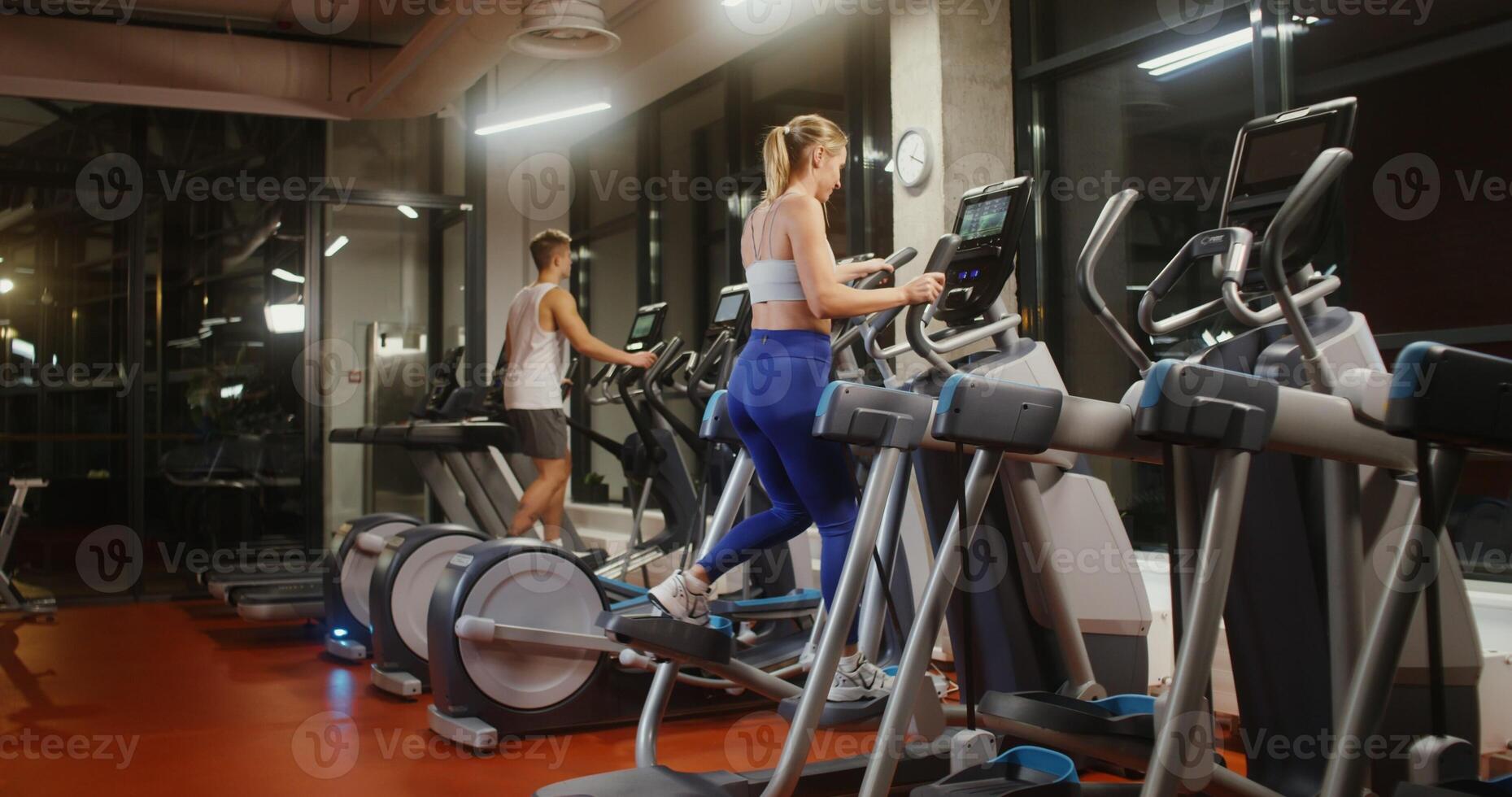 Young people a man and a woman of European appearance, dressed in sportswear, exercise on an ellipse in a well equipped indoor gym photo
