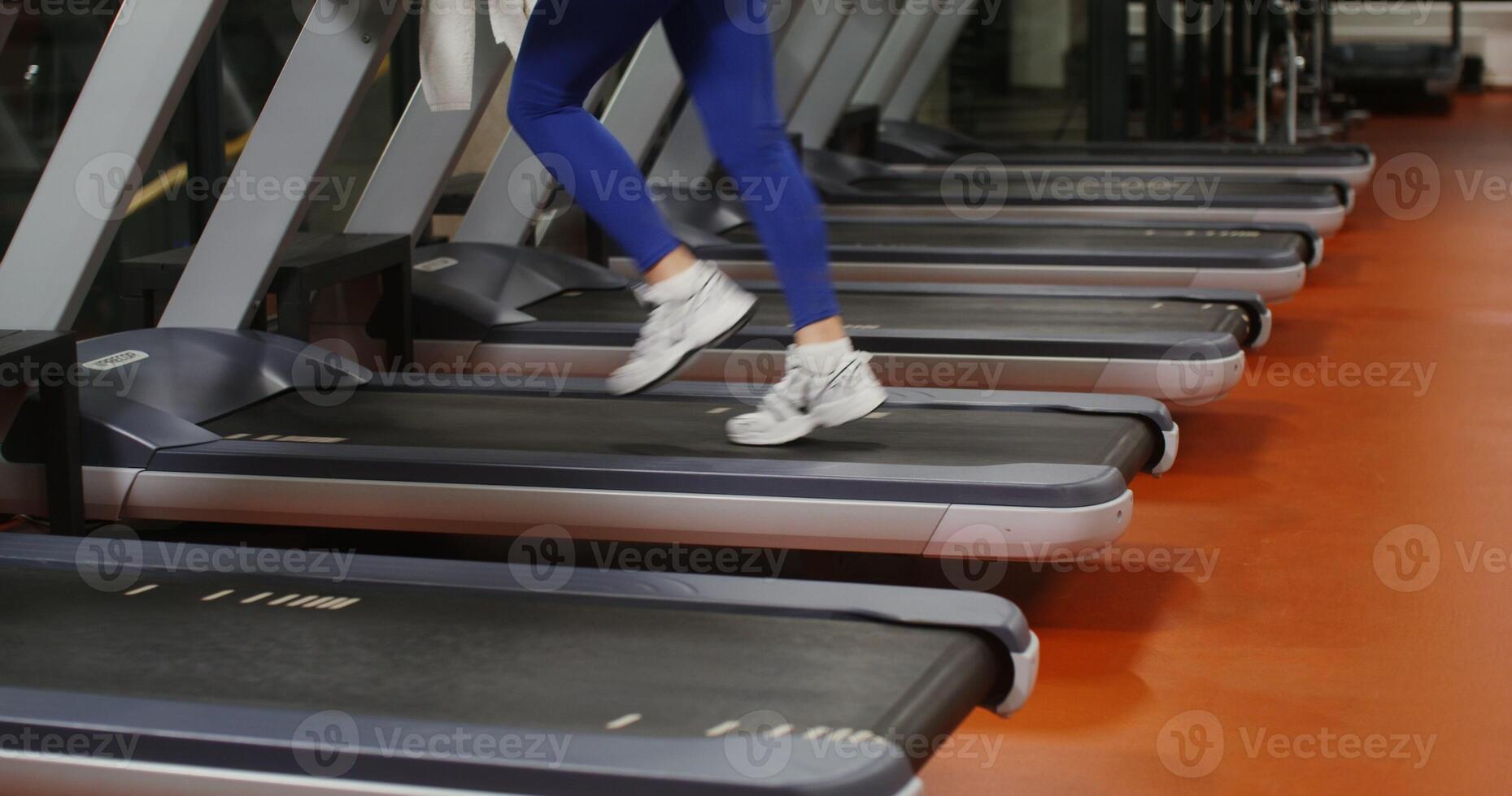 A woman in leggings and black and white sneakers runs on a treadmill, exercising in the gym, close up of female legs, the woman's face is not visible photo