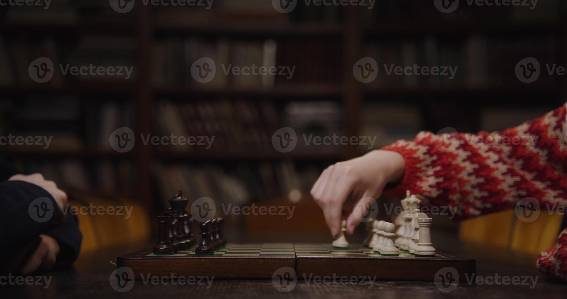 A man and a woman start a chess game, sitting opposite each other at a table in the library, close up of a chessboard photo