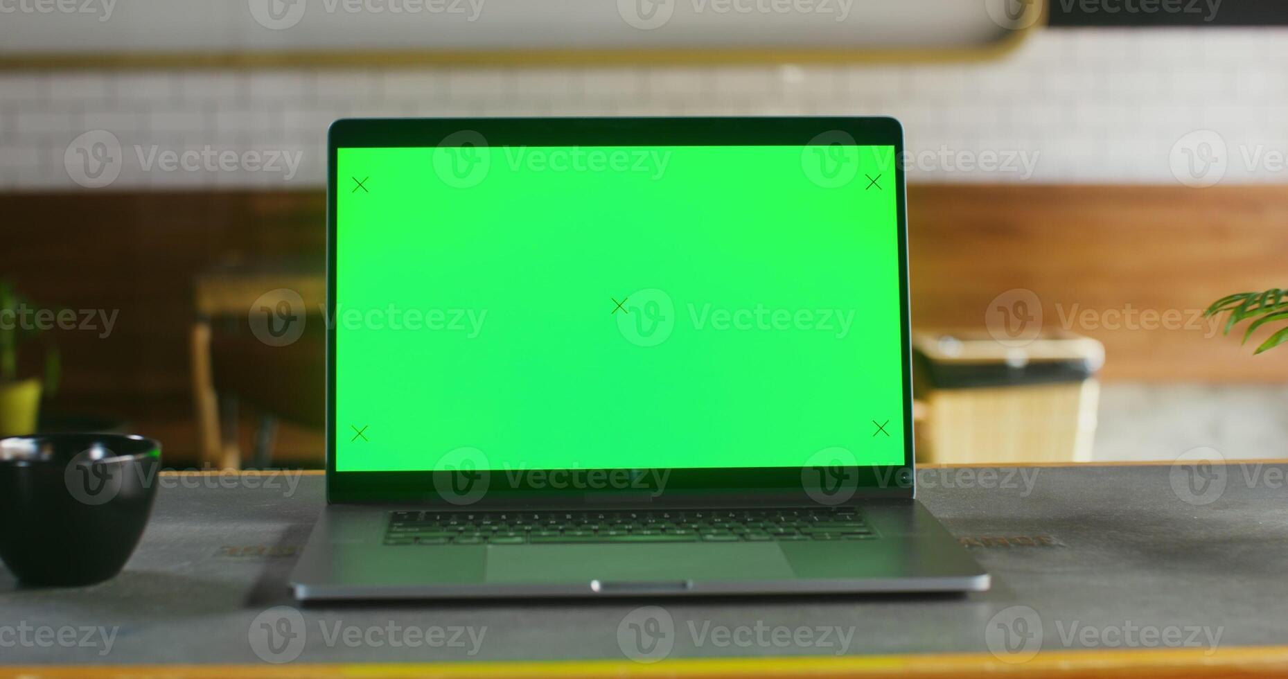 Open laptop with a green screen stands on a table in coffee shop open laptop with a green screen stands on a table in a coffee shop, close up. There are no people in the frame. Chrome key, copy space photo