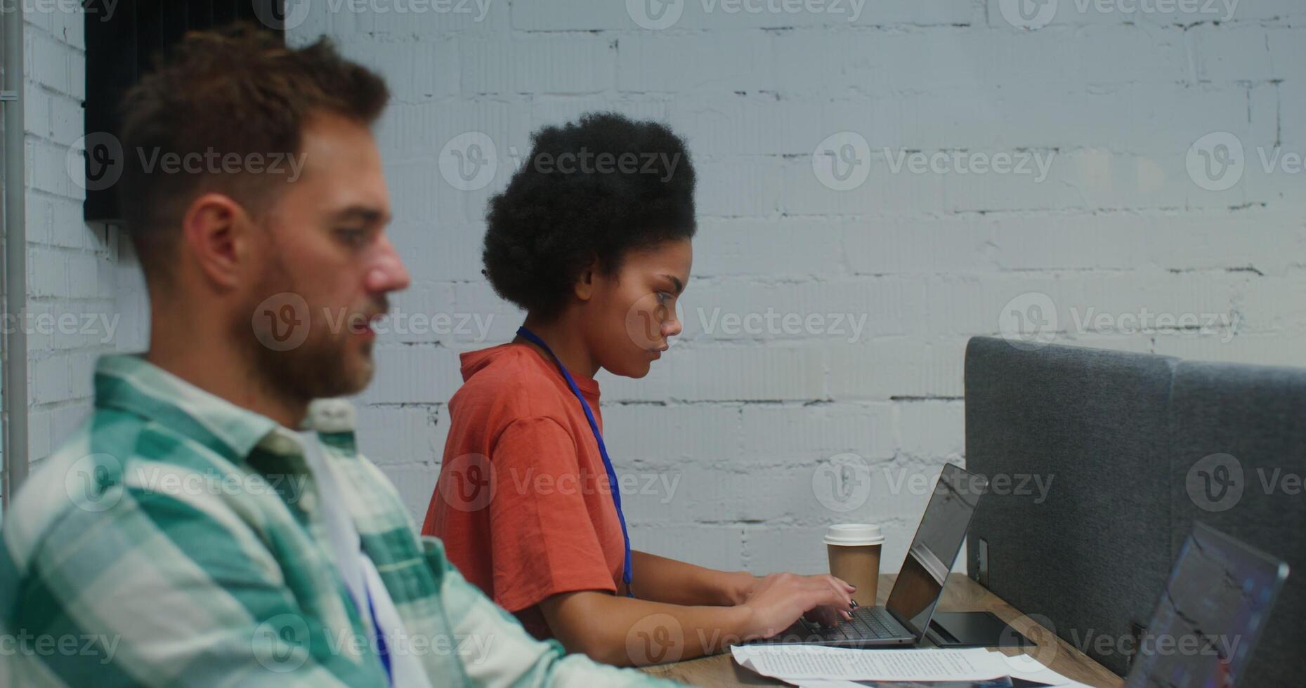 A young man of European appearance and an African American woman with a serious look work at laptops, sitting at one work table in a stylish office. 4K , red komodo photo
