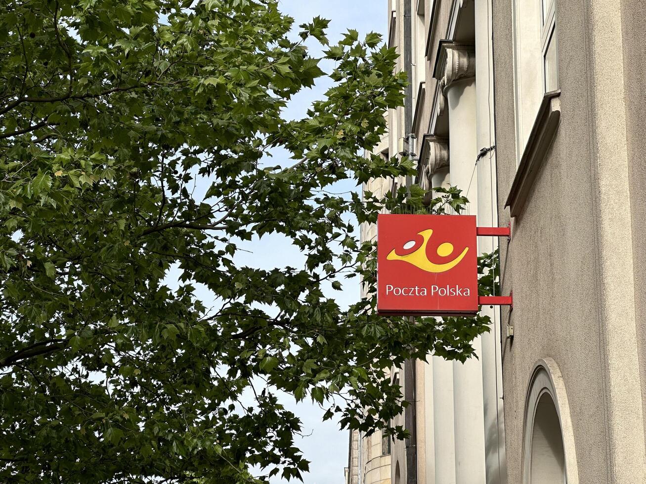 Warsaw, Poland - May 22, 2025 Sign of Poczt Polska postal service hangs on building facade surrounded by green leaves, showcasing urban life and postal services in Poland photo