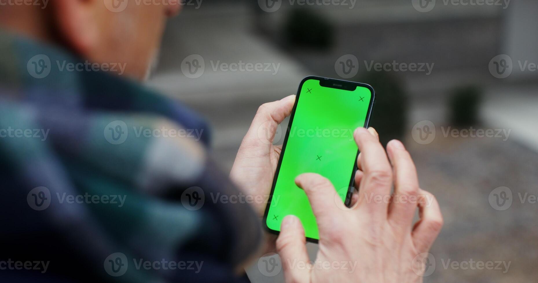 A warmly dressed man uses a phone with a green screen, swiping his finger across the screen, close up, top view from behind the man's shoulder. Chroma key, mockup. in 4k, red komodo photo