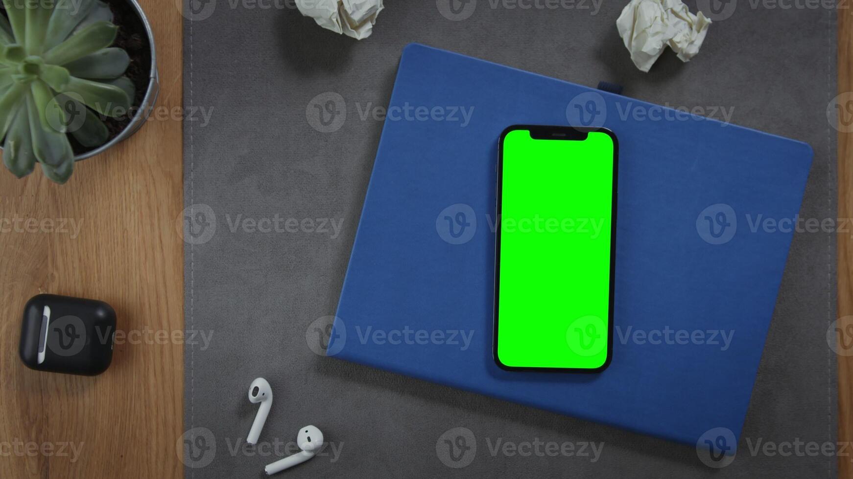 A man puts a cup of hot coffee on the desktop next to a mobile phone with a green screen lying on a notebook with crumpled pieces of paper nearby, close up. Mockup, chroma key, copy space photo
