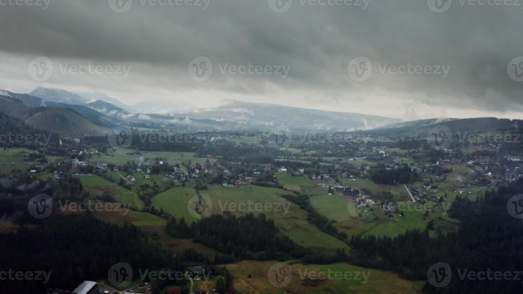 Vew of mountain valley with city in a lowland at foot of gently sloping mountains overgrown with a spruce forest covered with thick dark clouds photo