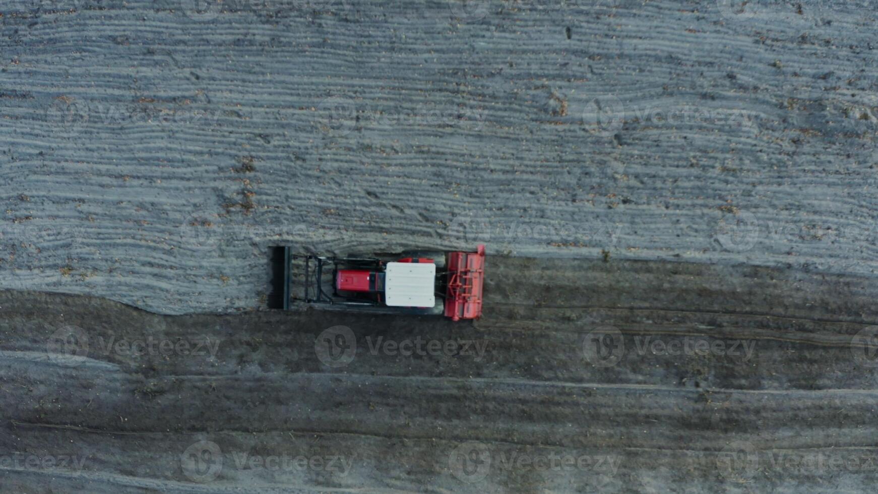 Red tractor with a plow plowing an agricultural field, drone aerial footage photo