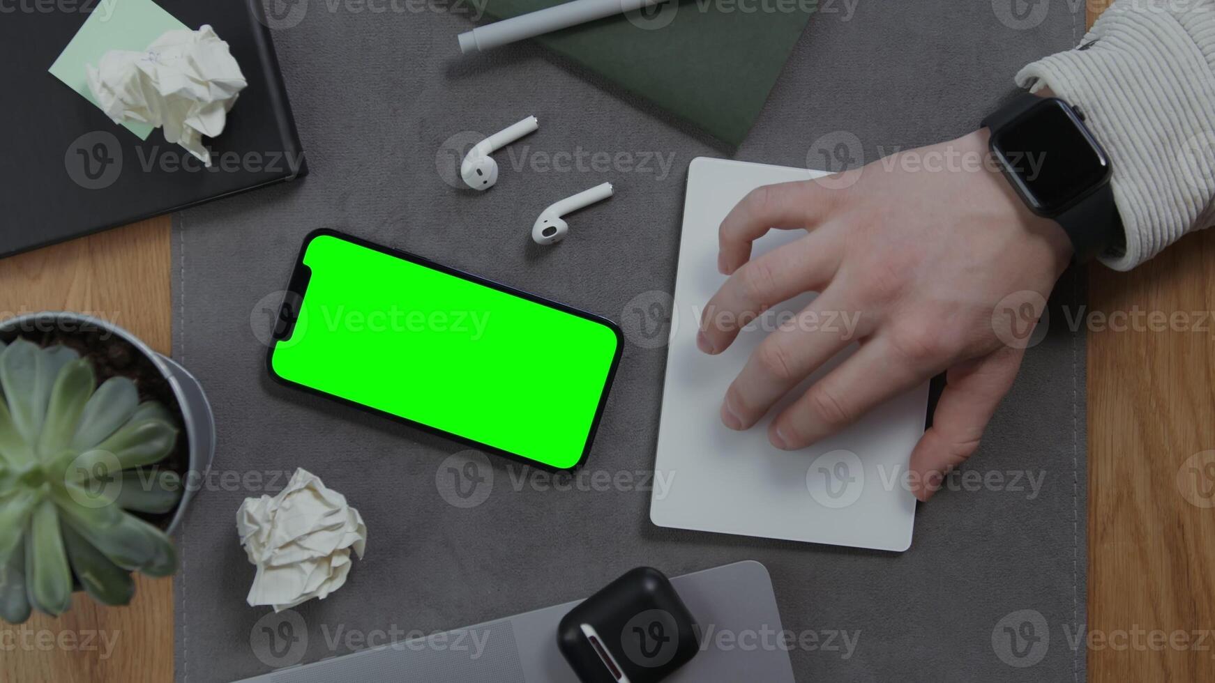 A man's hand lies on a blank sheet of notebook, next to a mobile phone with a green screen and crumpled sheets of paper, then takes the headphones, close up. Mockup, chroma key, copy space photo