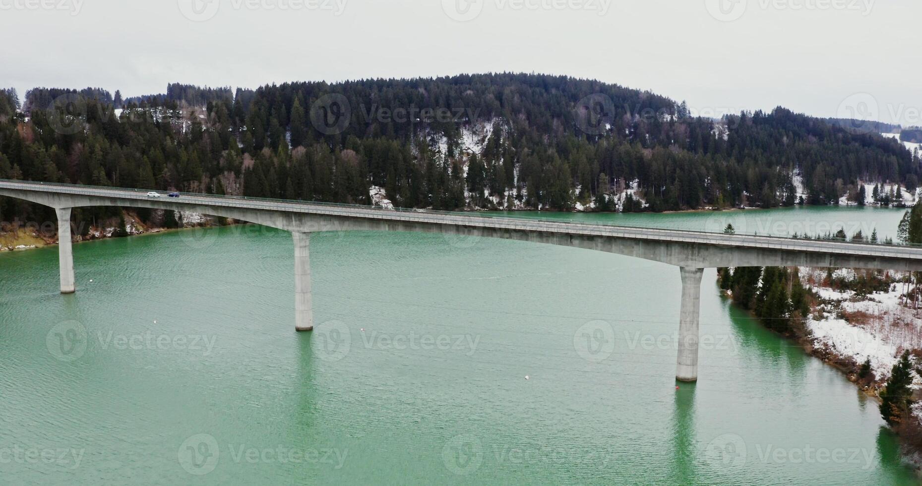 Beautiful winter landscape from bird's eye view, from a quadcopter. View of wide river flowing among spruce forests and fields covered with snow and narrow concrete road bridge connecting the banks photo
