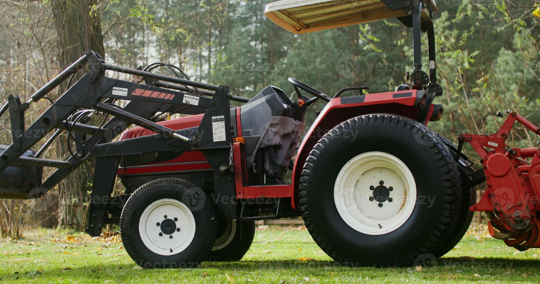 A modern agricultural tractor with a canopy above the driver's seat, with a bucket in front, stands at the edge of a field near the forest, close up photo