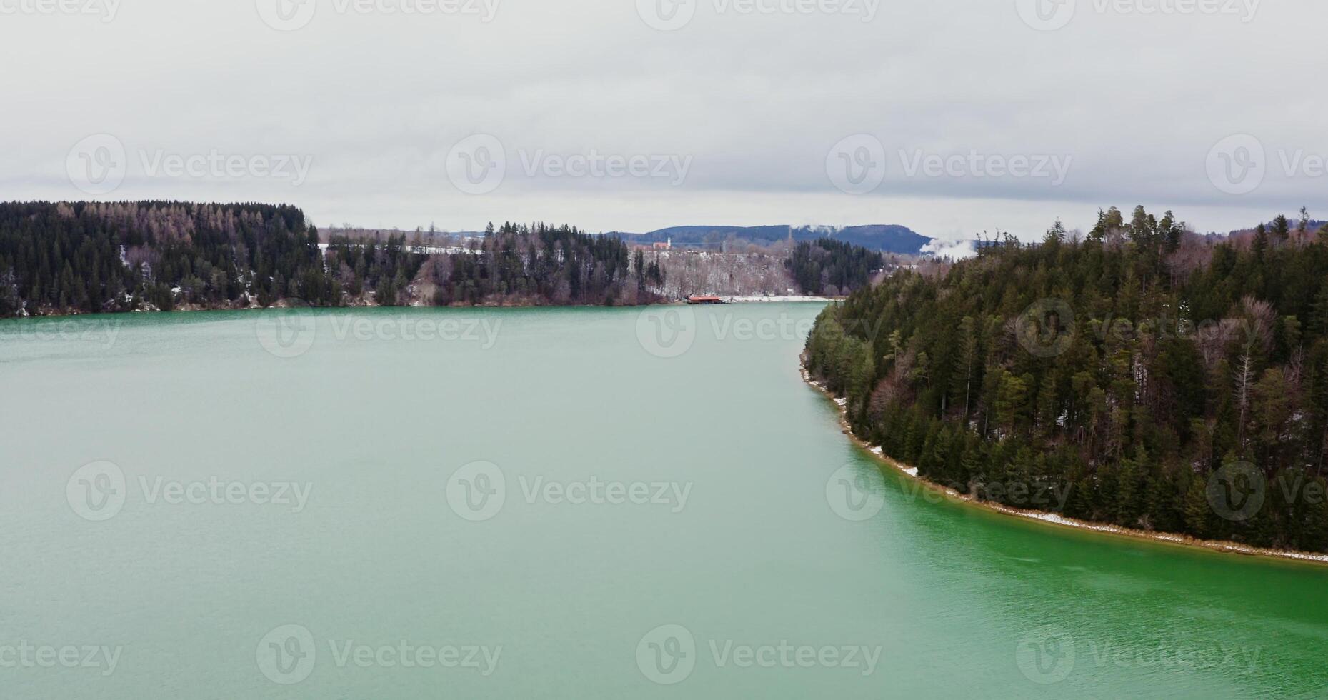 Beautiful winter landscape from bird's eye view. View of a wide river with small ripples of waves flowing through spruce forests and fields covered with snow. recording from a drone photo