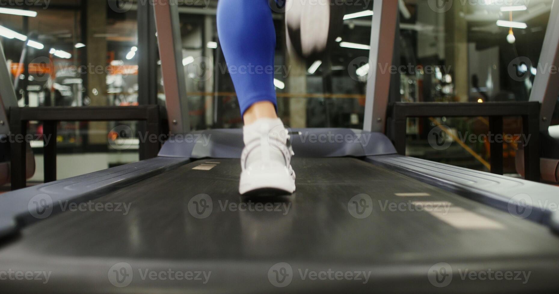 Close up of female legs in sneakers running on a treadmill, rear view. Beautiful footage of training on exercise equipment in the gym photo