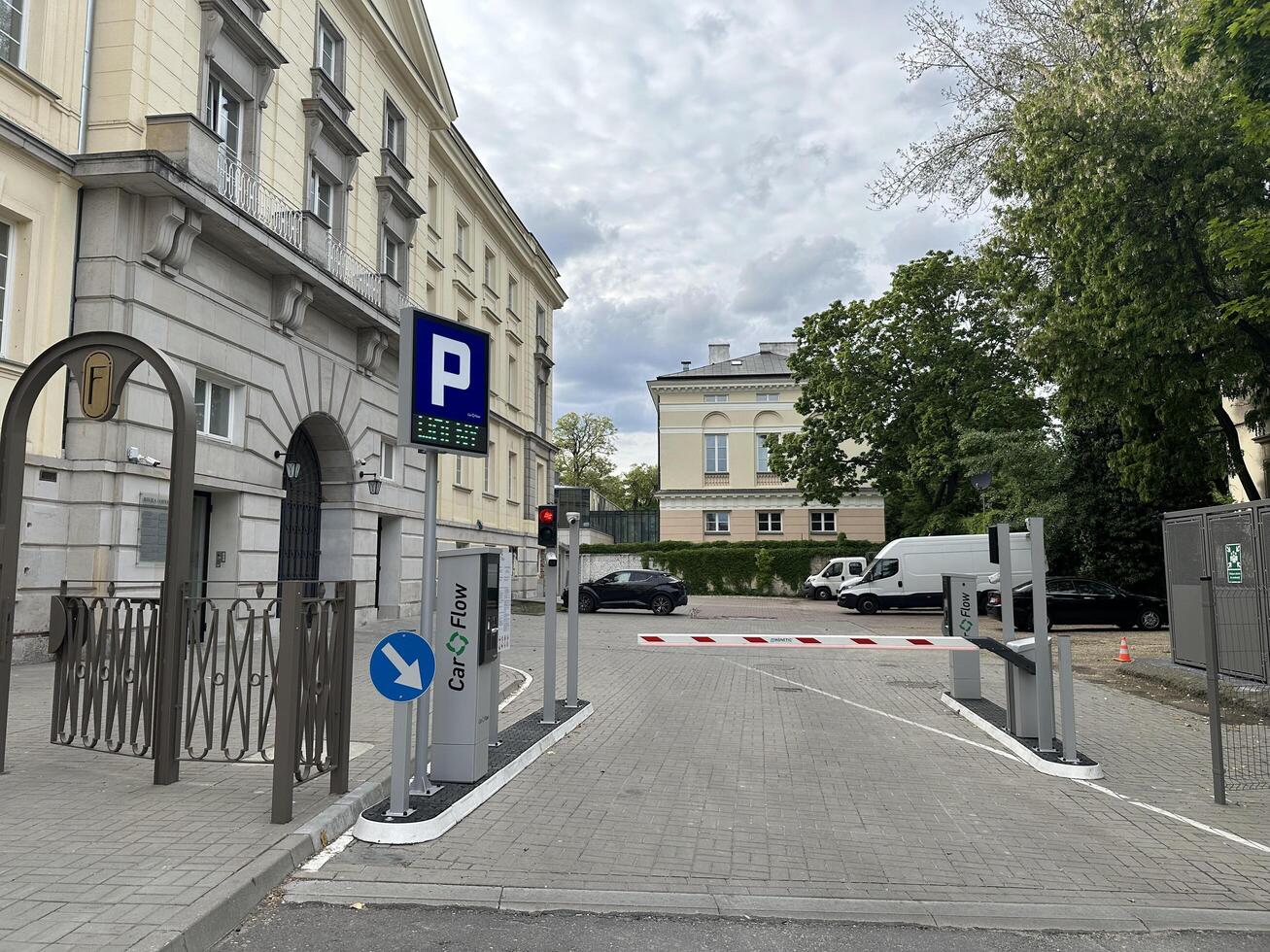 Warsaw, Poland - May 22, 2025 Parking entrance with automated gate and signage, surrounded by trees and historic buildings, showcasing urban infrastructure and accessibility photo