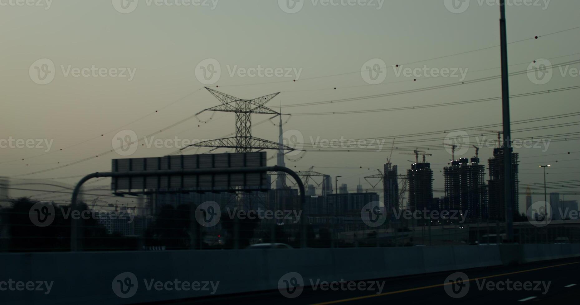 Busy highway on the outskirts of a modern metropolis with glass skyscrapers and many buildings under construction. Power lines above the road photo