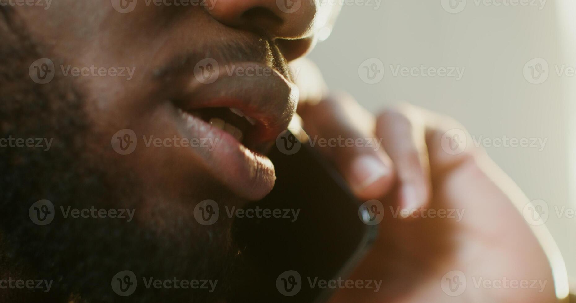 A young African American man with a beard is talking on a mobile phone with a serious look. Close up of plump male lips. in 4k, red komodo photo