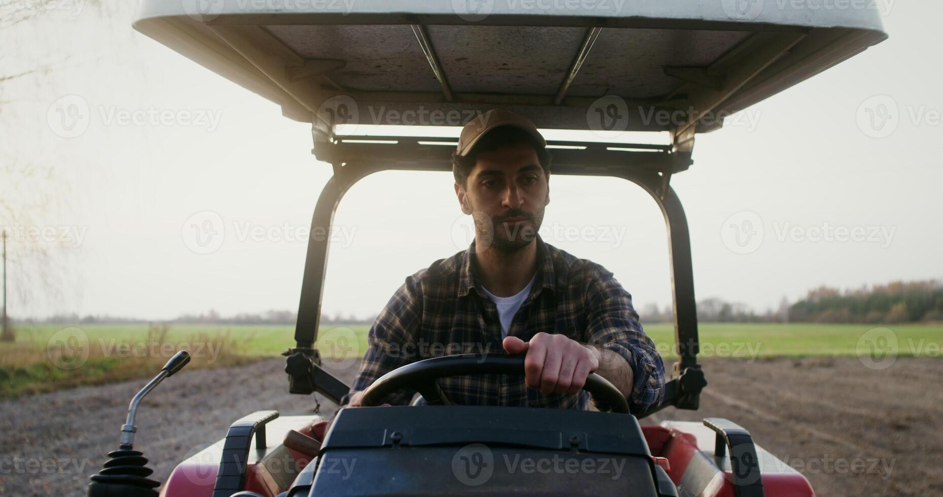 Close up front view of a tractor driver a young man of European appearance, with black hair and a beard with a serious view sitting at the wheel of an agricultural machine photo