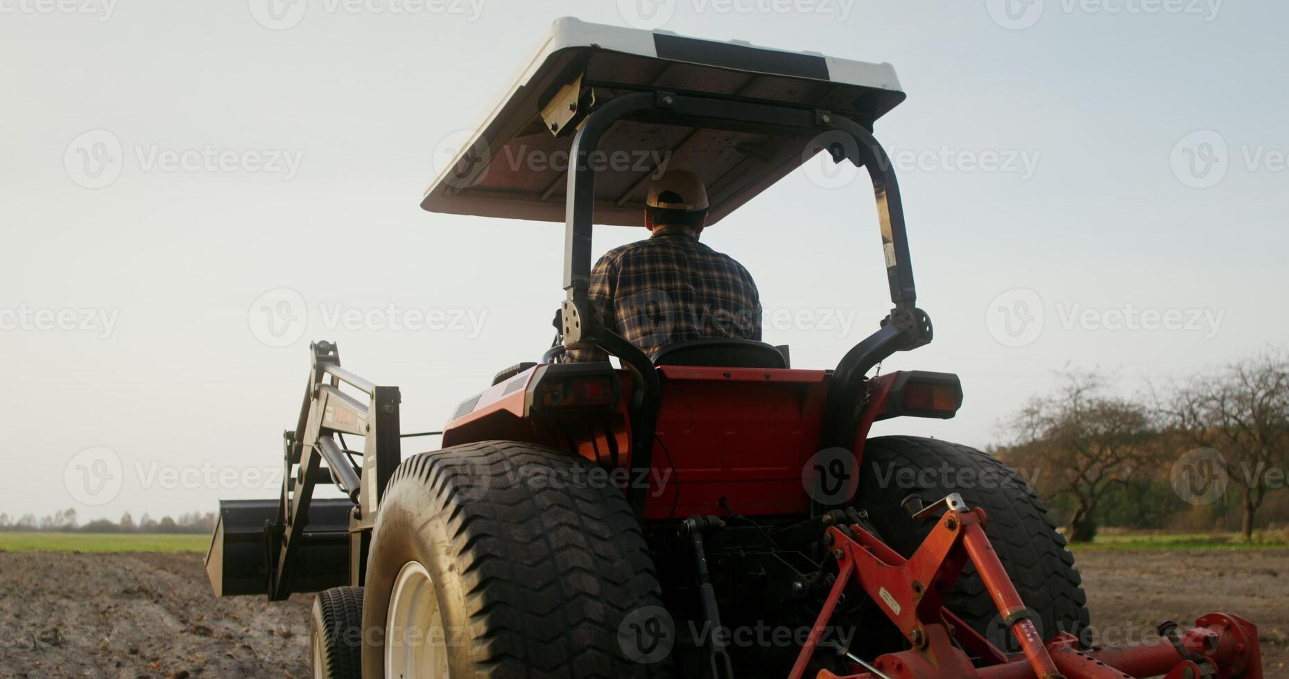 A young European looking farmer turns a tractor around and begins to drive along a new row, plowing a field on an autumn day and turns around, checking the quality of work photo