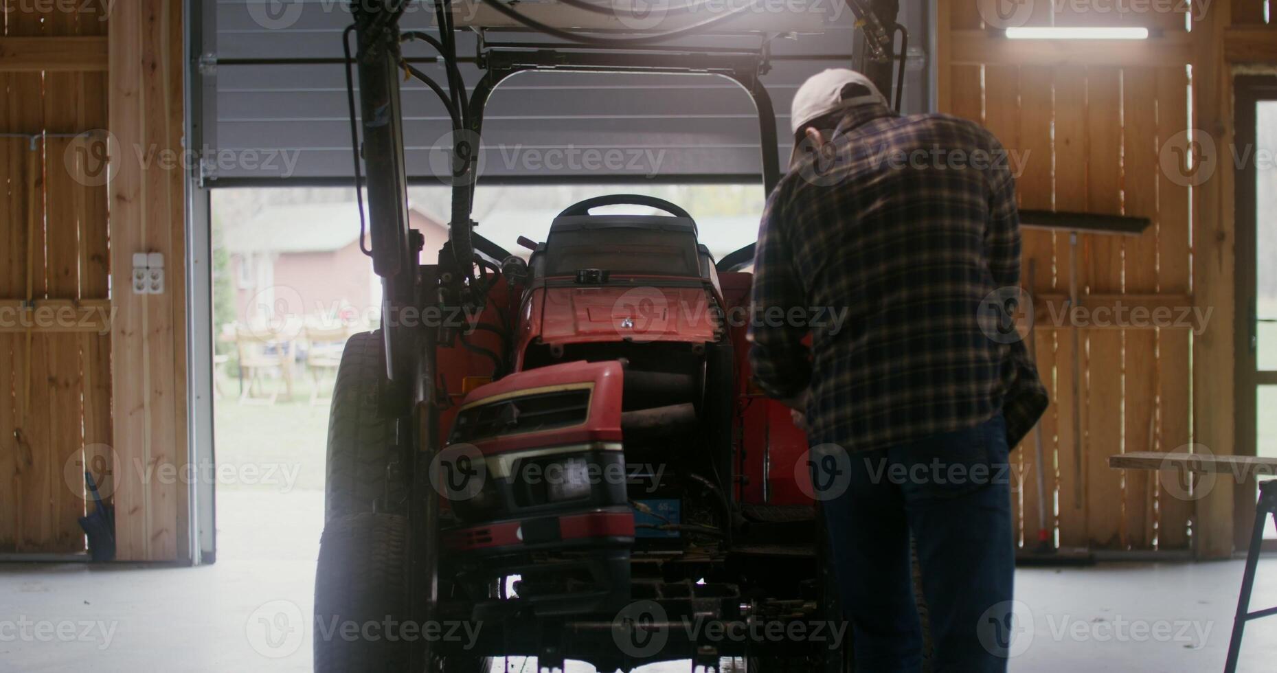 Young farmer a man of European appearance, with a beard tries to repair a small agricultural tractor on his own in a garage on a modern farm on an autumn day photo