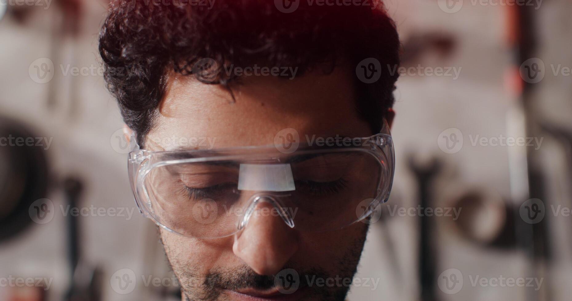 A close up of the face of a young man in protective glasses who looks up from a digital tablet and looks up at the camera with a smile. in 4k, red komodo photo