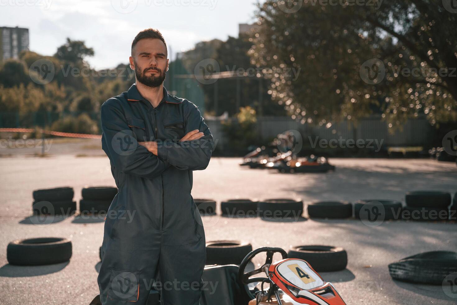 Standing against vehicle and trees. Man, is ,,outdoors, kart racing conception photo
