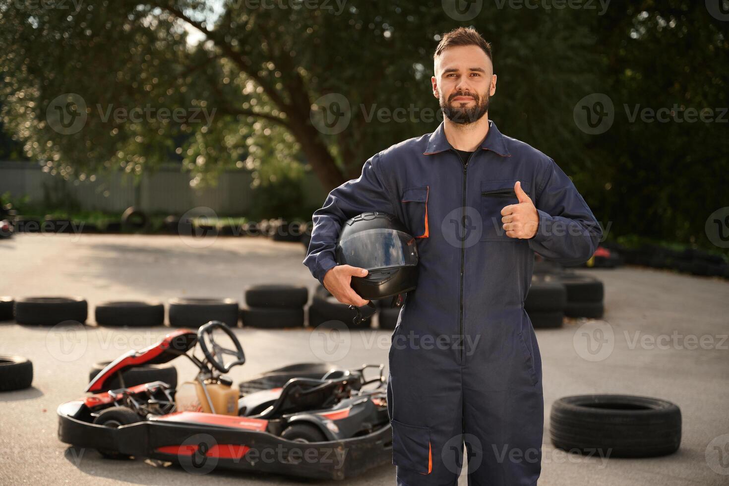 Standing, and holding safety helmet. Man is outdoors, kart racing conception photo