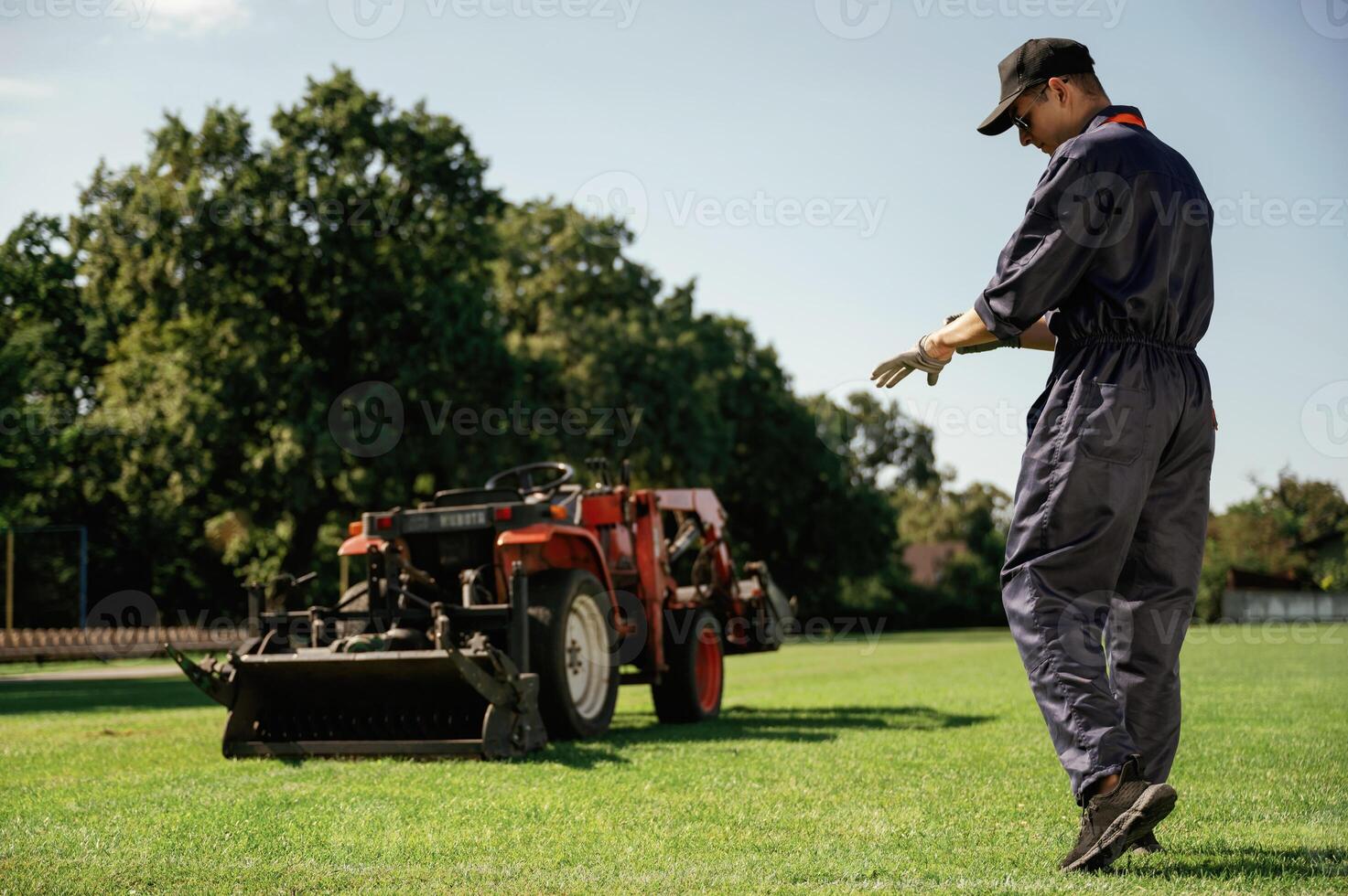 Rear, back view, walking... Man is with utility tractor with grass cutter and aerator equipment on the field photo