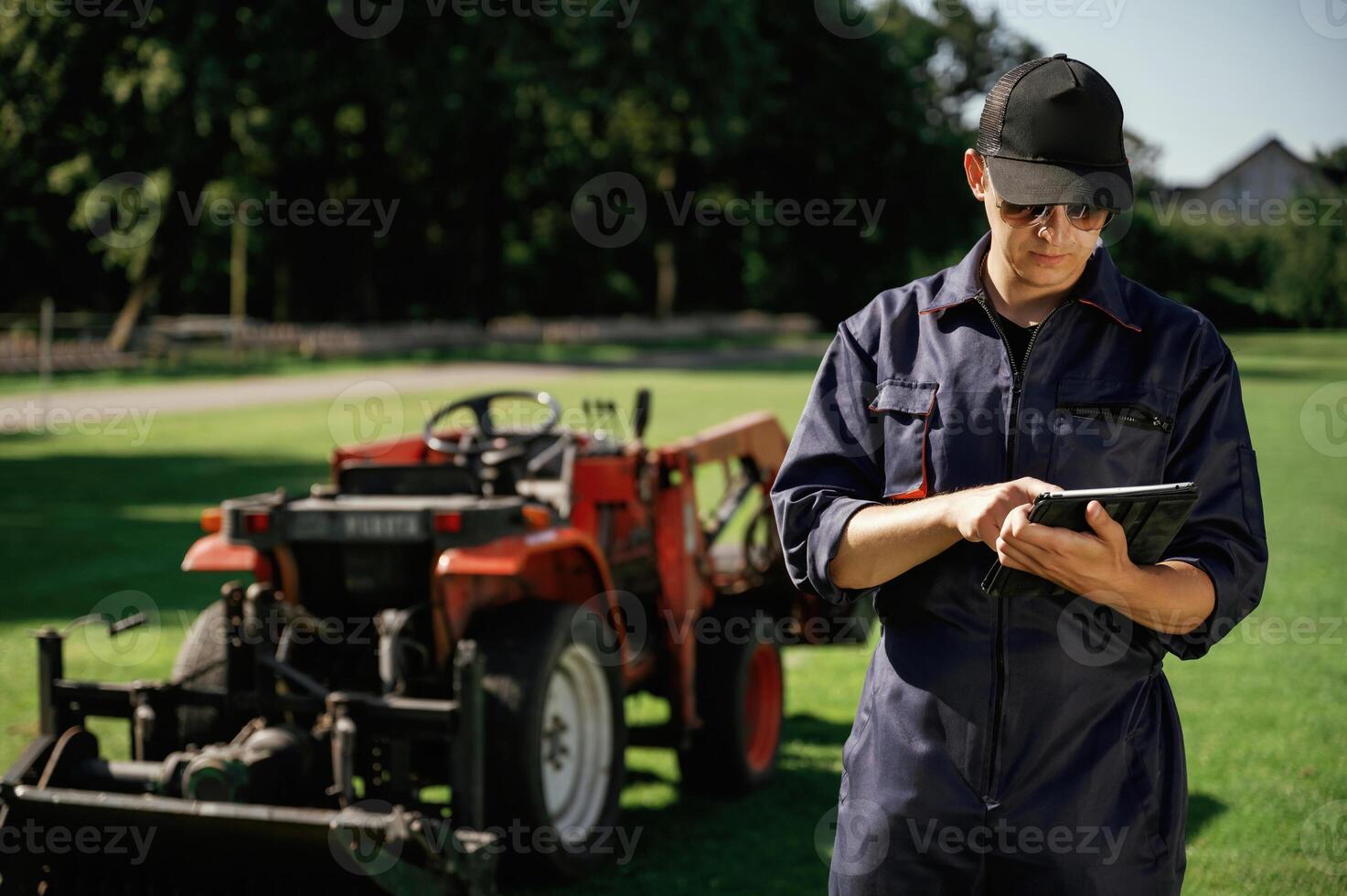 Black digital, tablet ,in hands. Man is with utility tractor with grass cutter and aerator equipment on the field photo