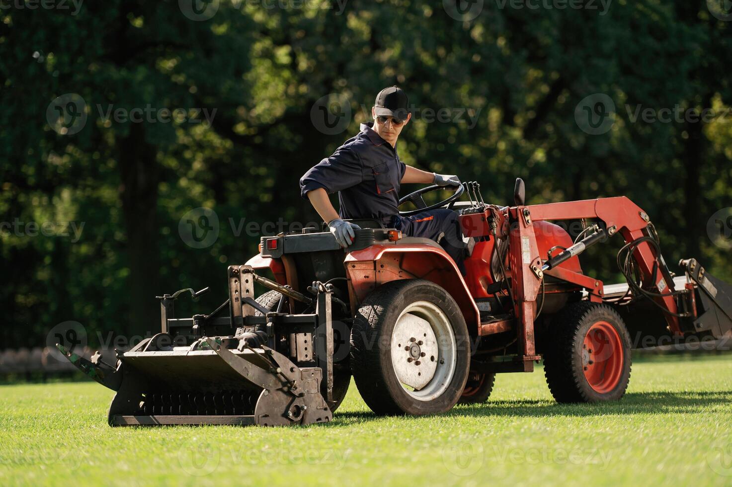 Sitting, and driving. Man is with utility tractor with grass cutter and aerator equipment on the field photo
