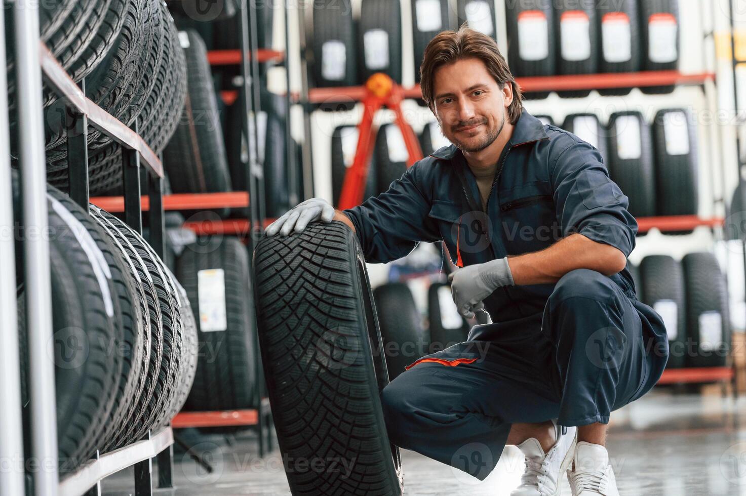 Sitting and showing the tire. Man is in the tire ,fitting car service photo