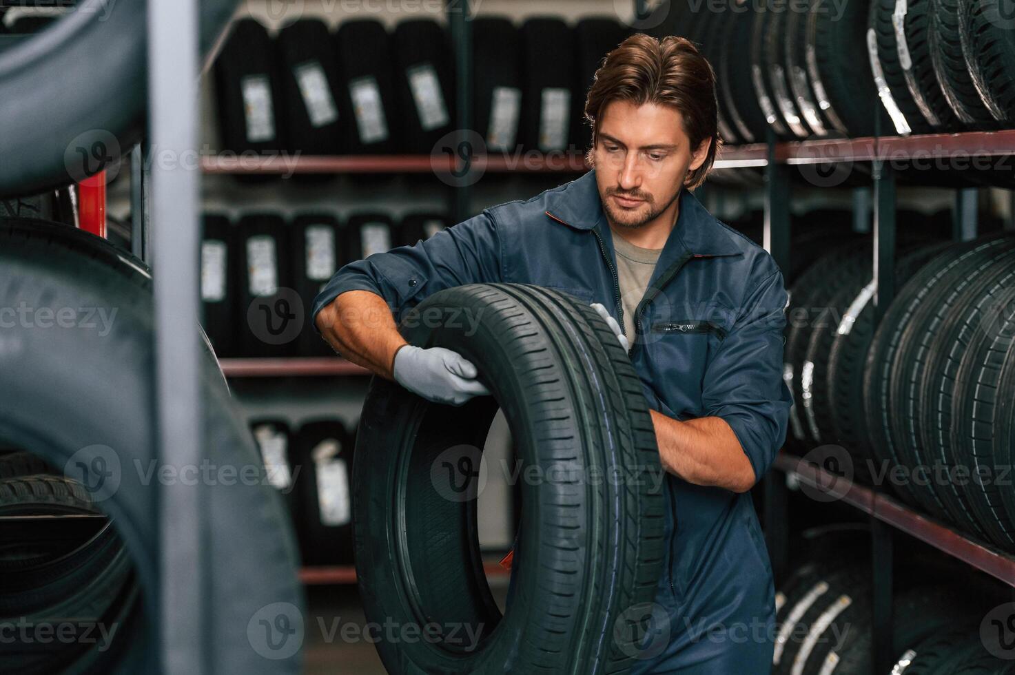 Indoors, holding tire.. Man is in the tire fitting car service photo