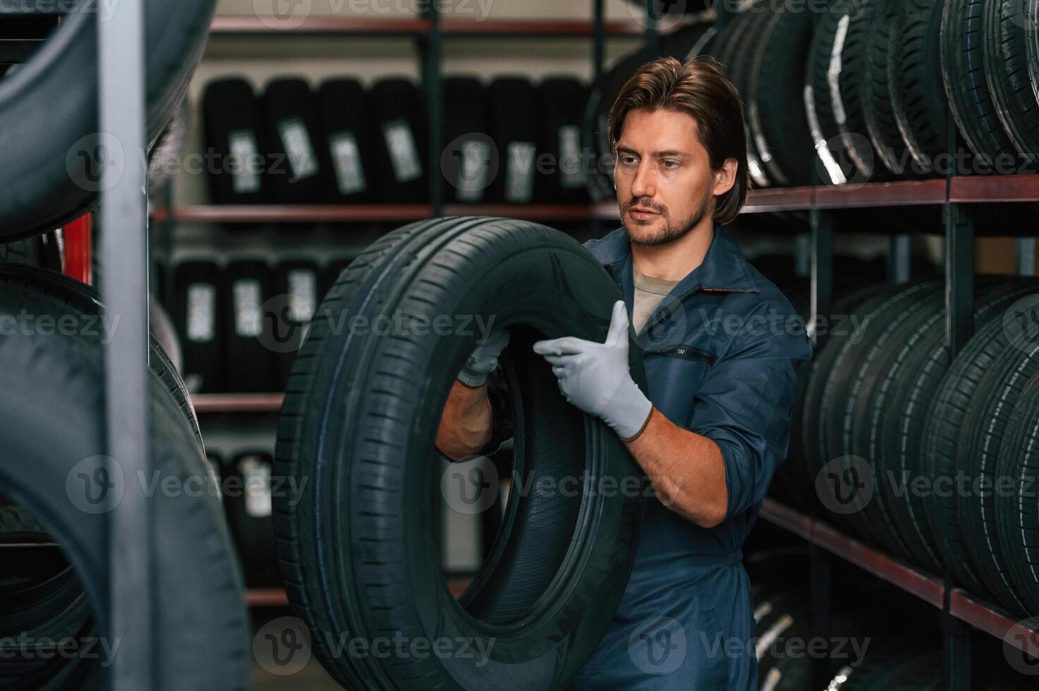 Indoors, holding tire. Man is ,in,, the tire fitting car service photo