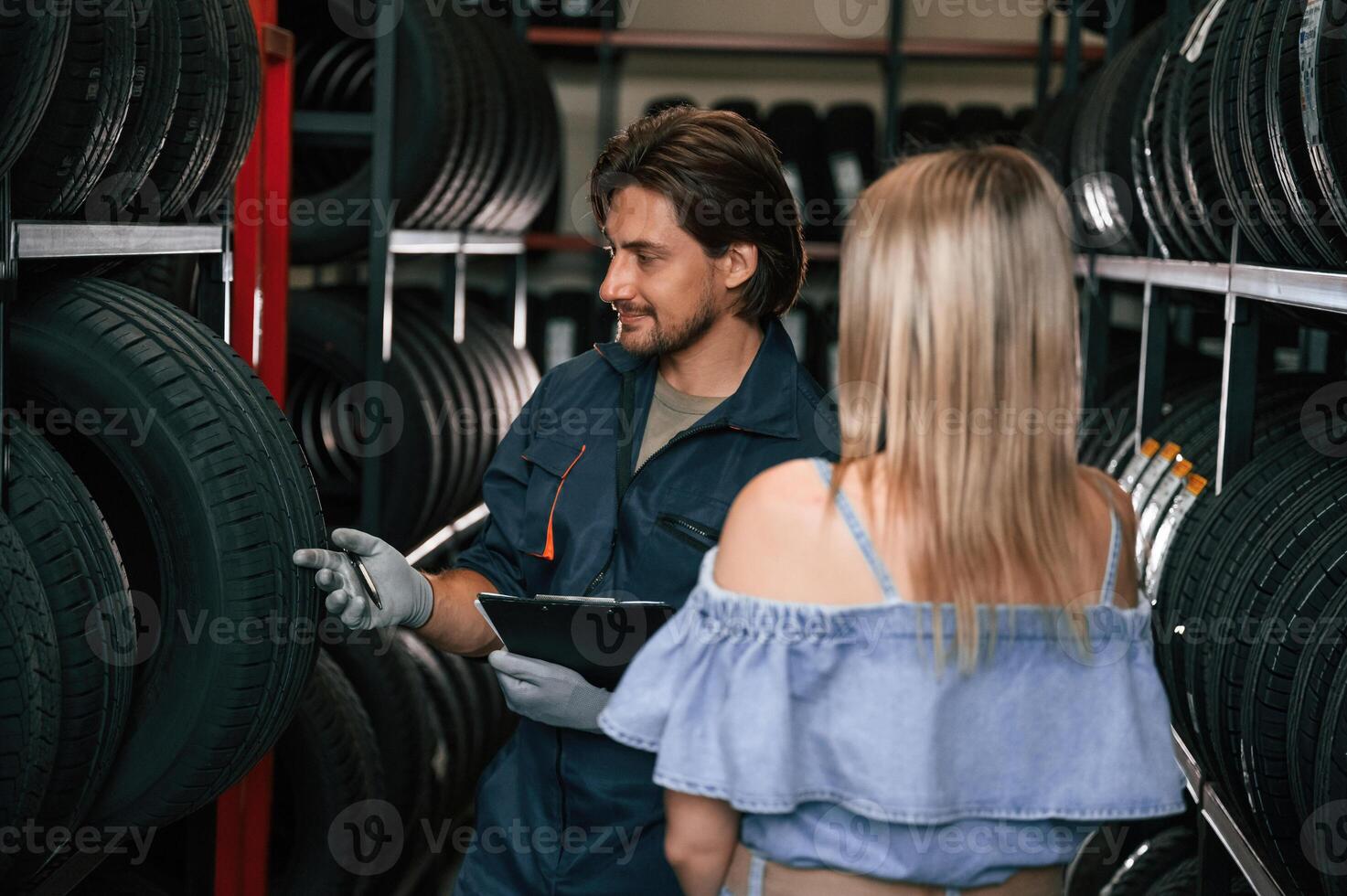 Giving the, advice. Woman is in the tire fitting auto shop with worker photo