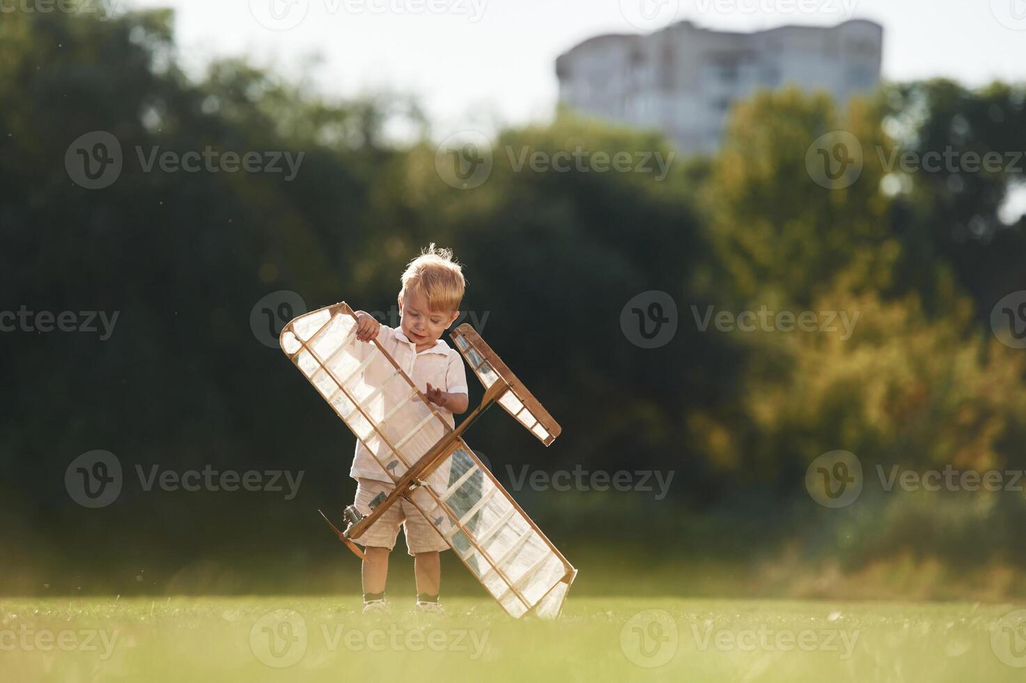 Holding ,it ,in ,hands. Cute little boy is playing with toy plane on the field.. photo