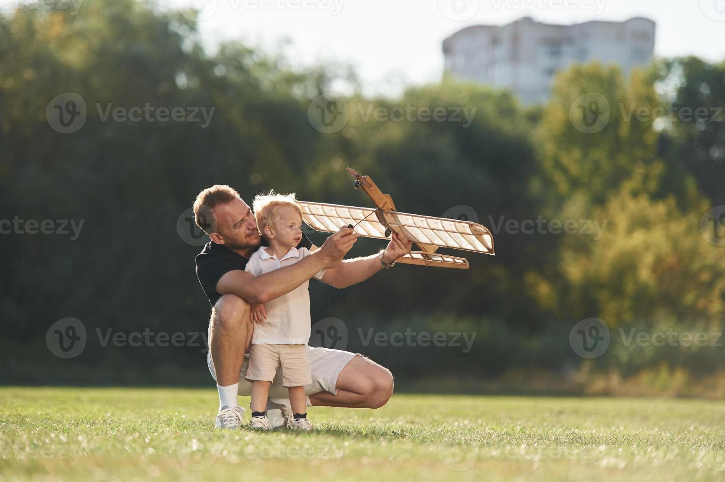 Screwdriver in hand, fixing it. Father and son are on the field together with toy plane, photo