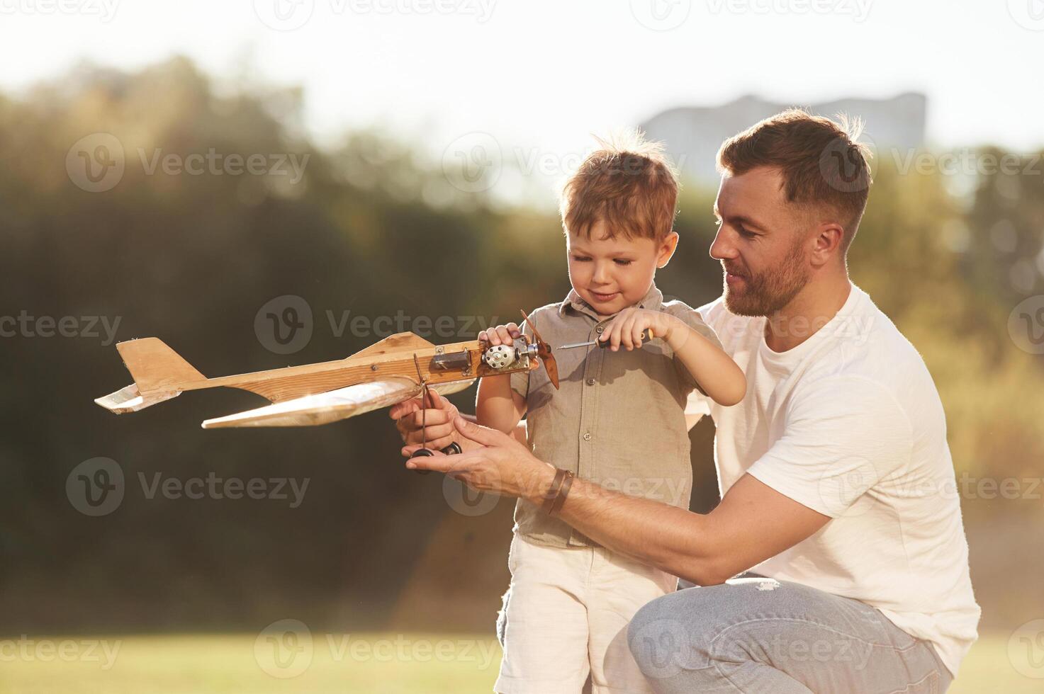 Fixing, using screwdriver. Father and son are on the field together with toy plane., photo
