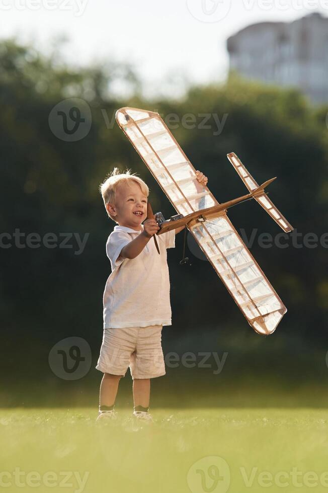 Holding,, it ,in, hands. Cute little boy is playing with toy plane on the field photo