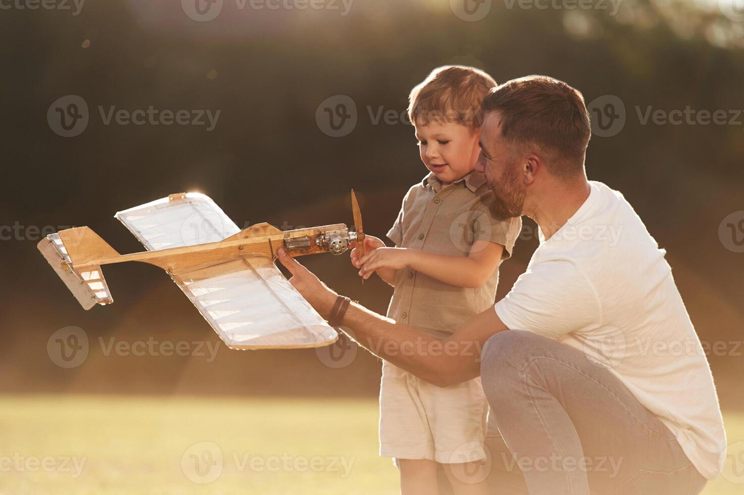 Illuminated, by sunlight, fixing broken toy. Father and son are on the field together with plane photo